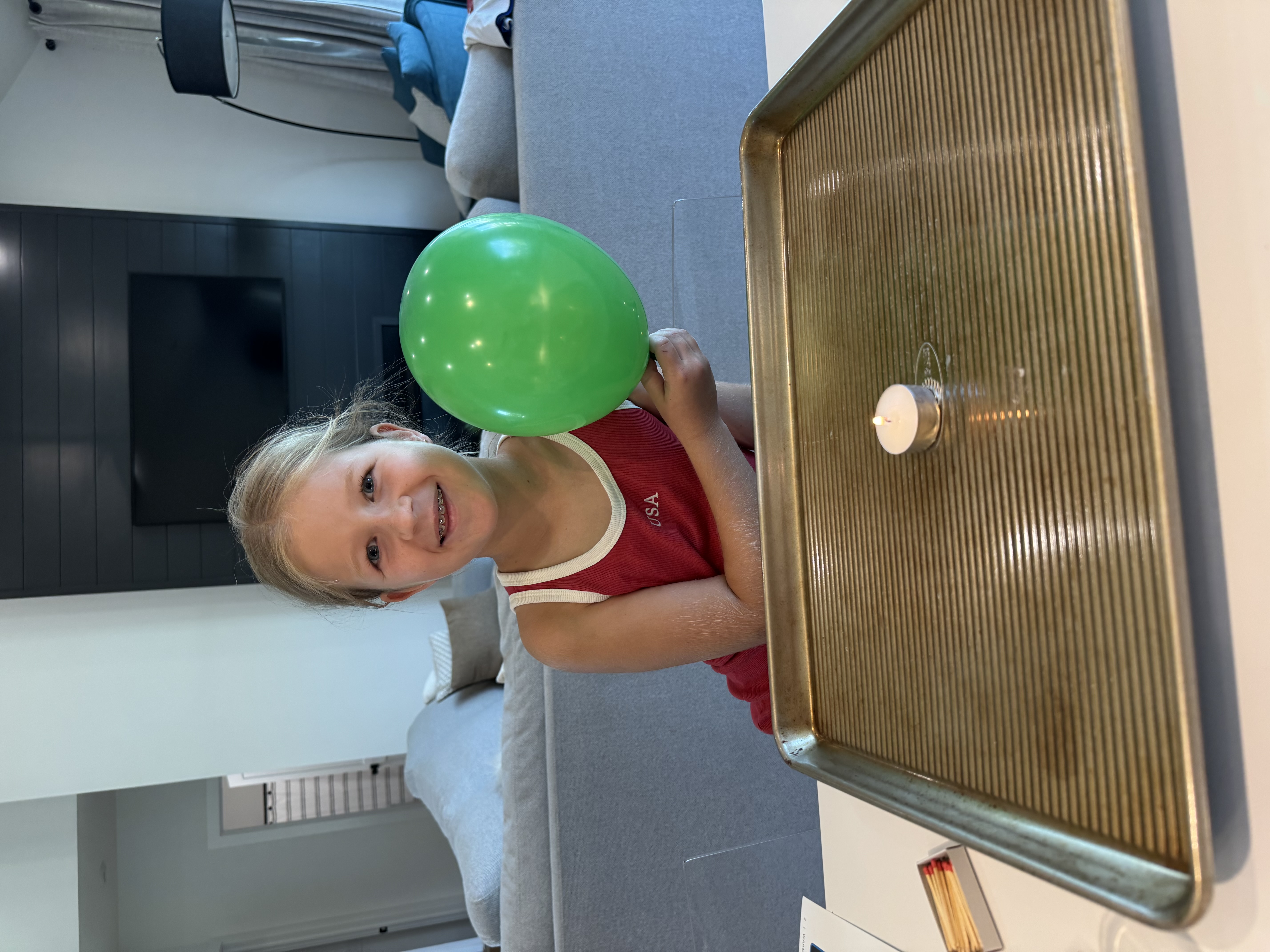 Holding a green balloon next to a candle on a tray
